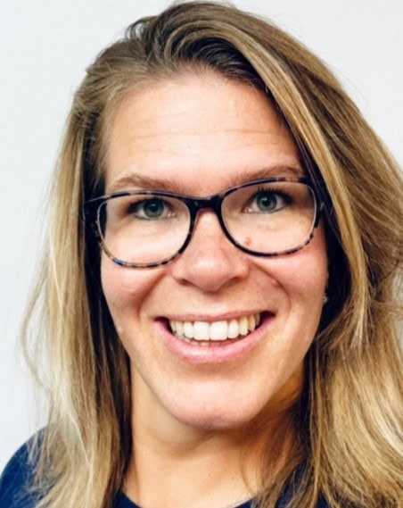 Vriendelijke vrouw met bril en lange blonde haar, glimlachend voor witte achtergrond.