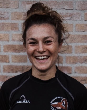 Vrolijke vrouw met sportkleding voor een bakstenen muur.